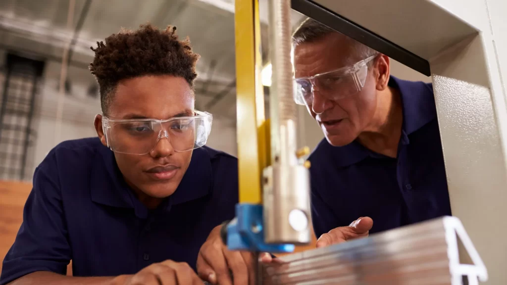 Carpenter Training Male Apprentice To Use Mechanized Saw