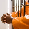 cropped image of prisoner with hands in prison bars