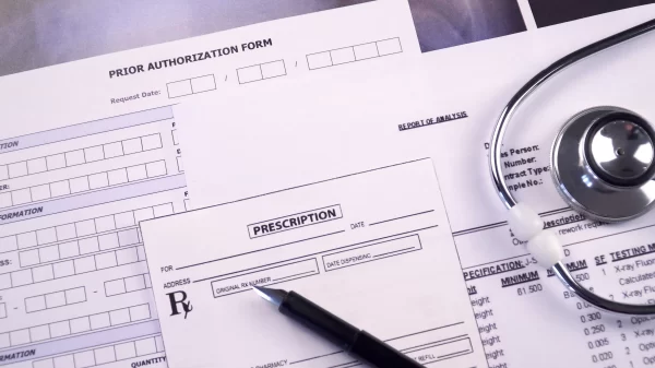 Prior authorization form, report of analysis form, x-ray picture and prescription blank next to the stethoscope and pen