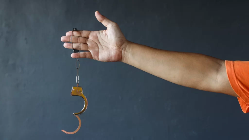 Hand of prisoner man wearing orange clothes holding opened handcuffs. Free from jail or freedom concept