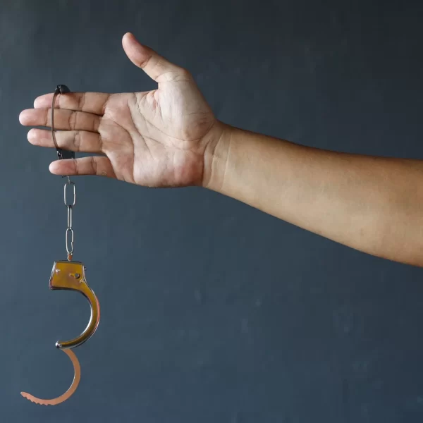 Hand of prisoner man wearing orange clothes holding opened handcuffs. Free from jail or freedom concept