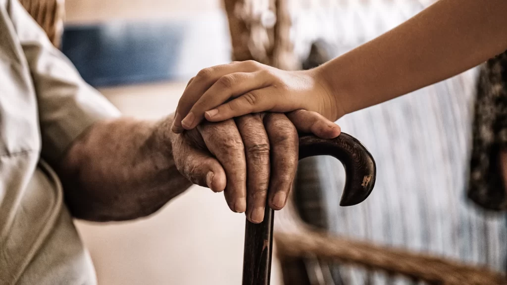 child's hand over old man's hand holding a cane.