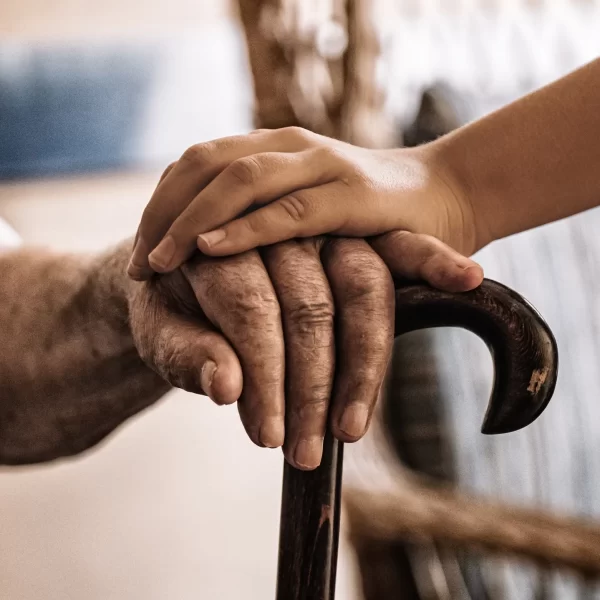 child's hand over old man's hand holding a cane.