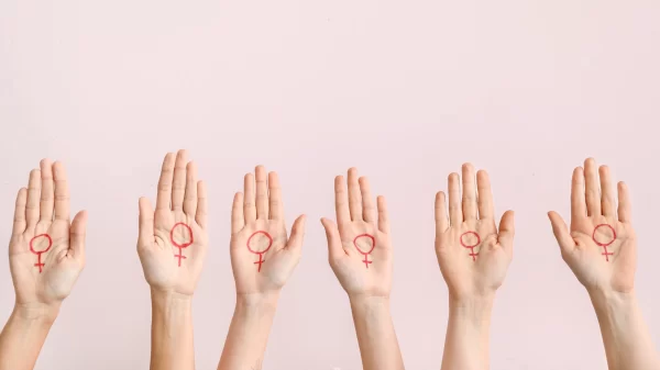 Women with drawn symbols of woman on their palms against color background. Concept of feminism