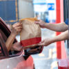 Hand Man in car receiving coffee in drive thru fast food restaurant. Staff serving takeaway order for driver in delivery window. Drive through and takeaway for buy fast food for protect covid19.