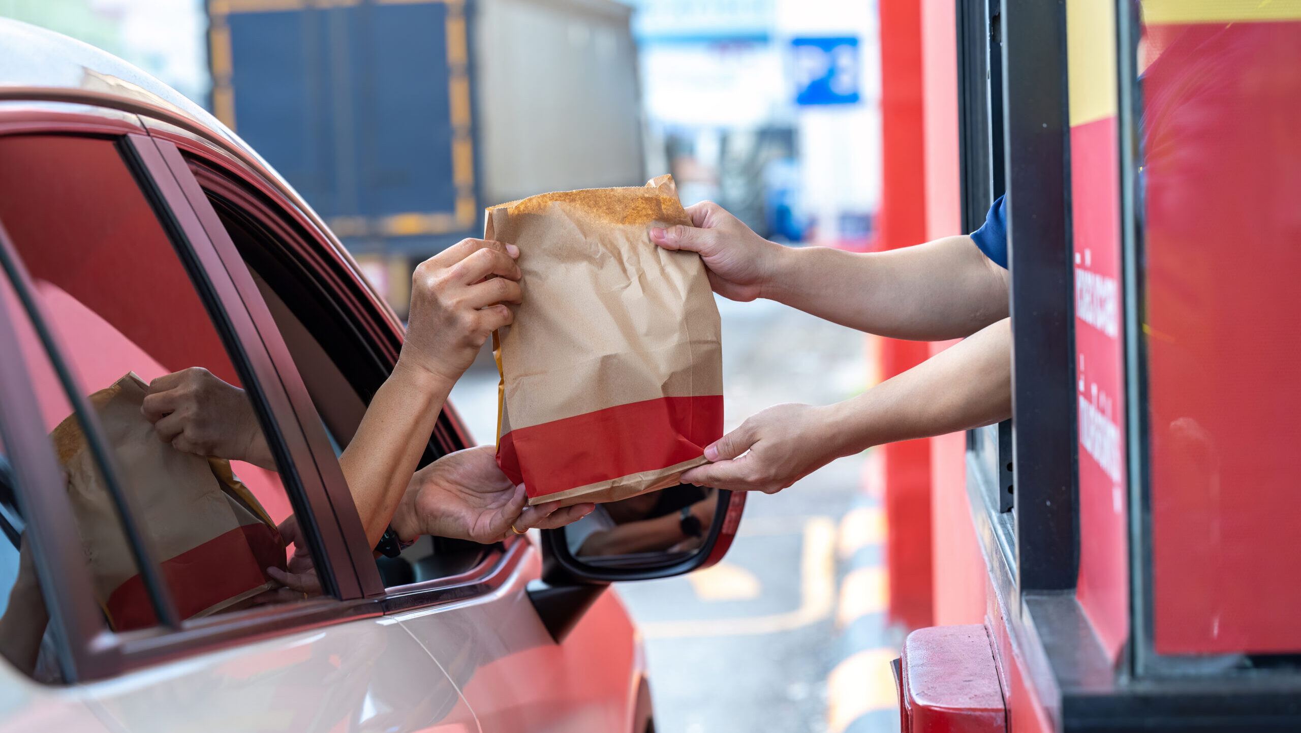 Hand Man in car receiving coffee in drive thru fast food restaurant. Staff serving takeaway order for driver in delivery window. Drive through and takeaway for buy fast food for protect covid19.