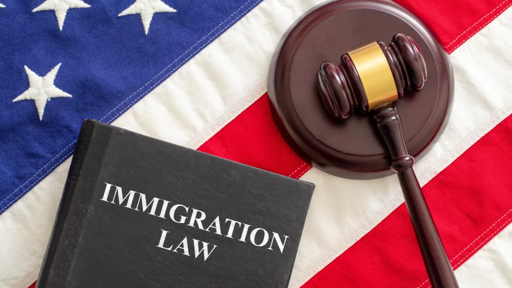 Immigration law text on black book and judge gavel on US of America flag background, top view. Migration, emigration visa in USA concept