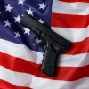 Black pistol lies against the background of the American flag. Personal weapons of the population. Close-up. Permission to carry weapons. Self-defense. Concept of protecting personal property and life