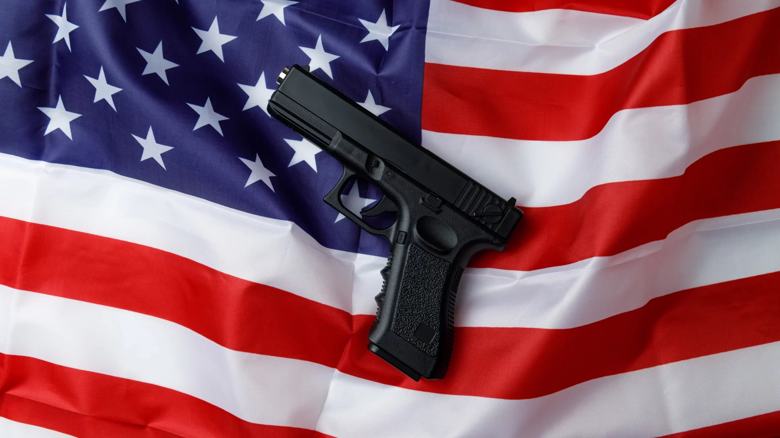 Black pistol lies against the background of the American flag. Personal weapons of the population. Close-up. Permission to carry weapons. Self-defense. Concept of protecting personal property and life